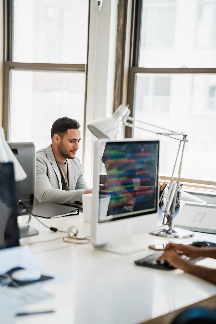 A young man working at a desktop computer in a bright, modern office environment.